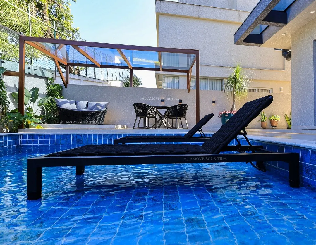 Espreguiçadeiras em tricô náutico preto na borda da piscina com pergolado ao fundo