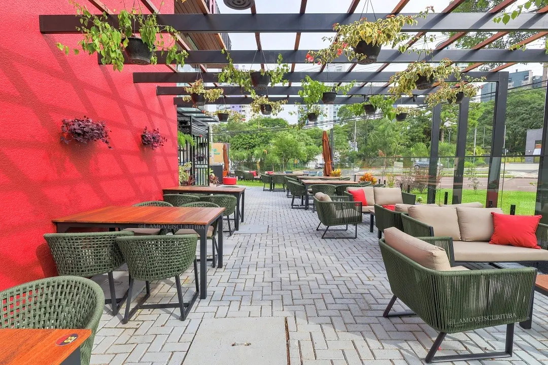 Terraço coberto por pergolado com poltronas em corda náutica verde, sofá com almofadas bege e mesa de jantar em Cumaru