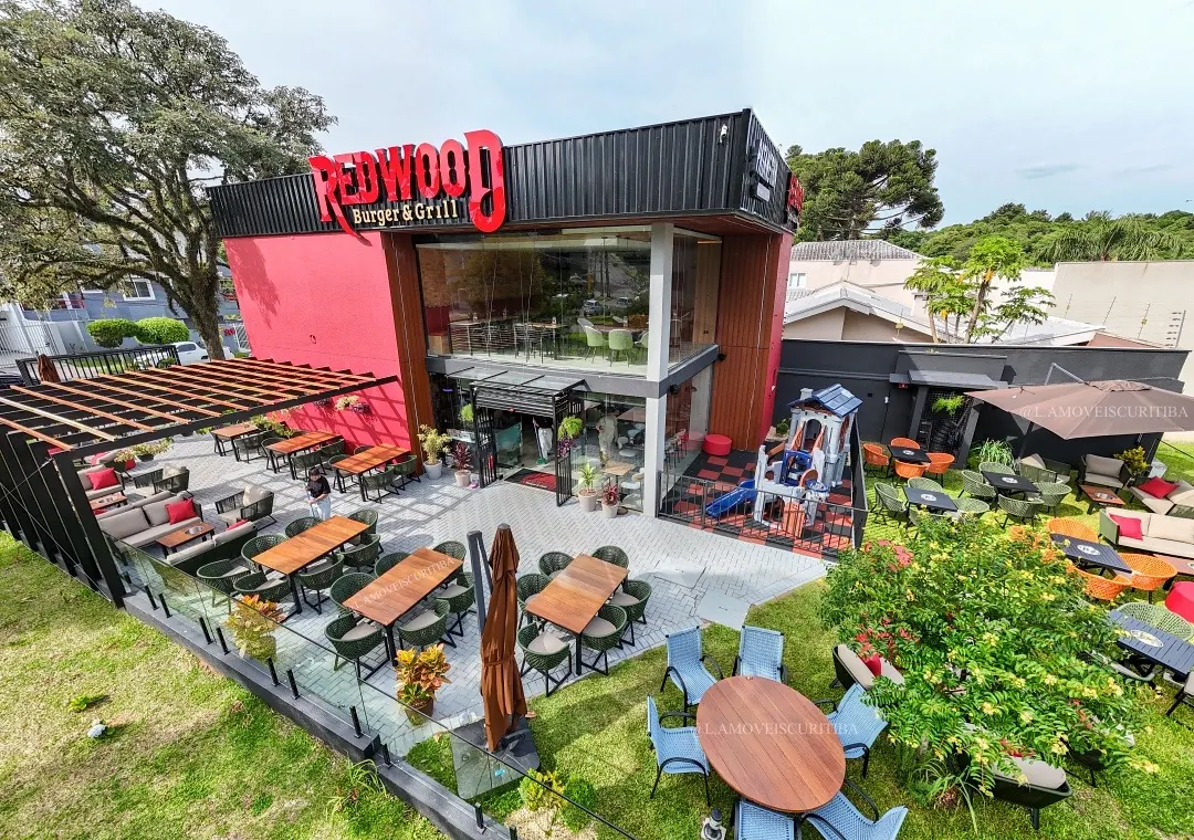 Vista aérea do restaurante com pergolado de madeira, mesas em Cumaru e lounges com poltronas no jardim